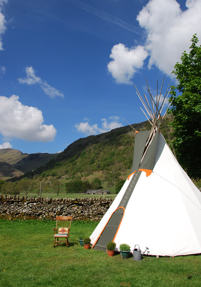 A tipi in the sun in the lake district with herbs and a watering can outside